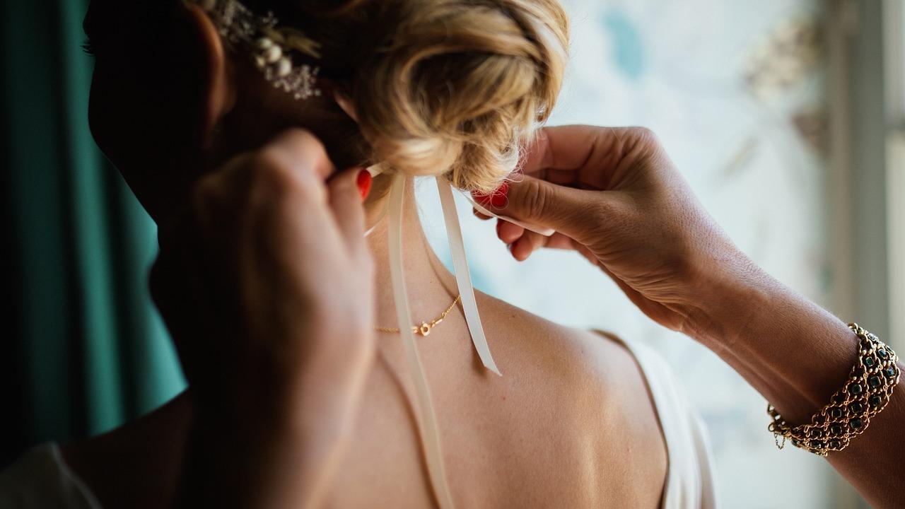 Hair stylist adjusting delicate white ribbons in a bride's updo hairstyle, captured in soft natural window light