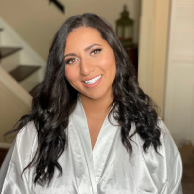 Radiant bride in white silk robe with lace trim, featuring glamorous waves in dark hair and natural glowing makeup during wedding preparations