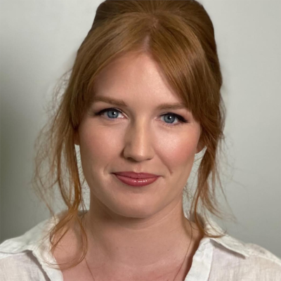 Bride with soft red hair styled in a romantic half-updo, wearing natural wedding makeup and a white blouse.