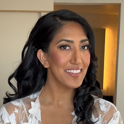 Bride with long black hair in soft curls, wearing natural glam wedding makeup and a white lace bridal robe.