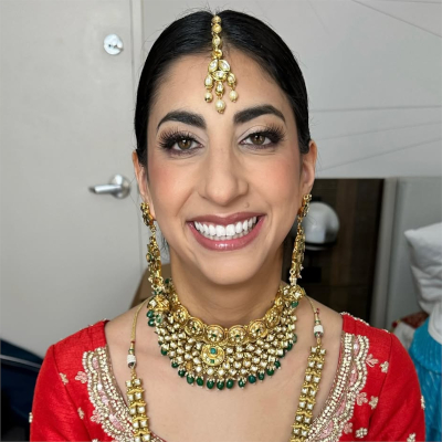 Bride in traditional red lehenga with gold embroidery, wearing elegant bridal makeup and ornate gold jewelry with emerald accents