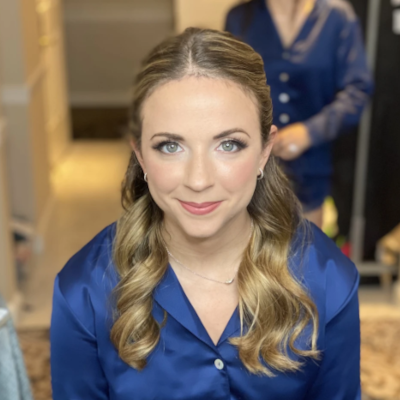 Bridesmaid with soft glam makeup and side-swept curls, wearing navy silk robe during wedding morning preparations